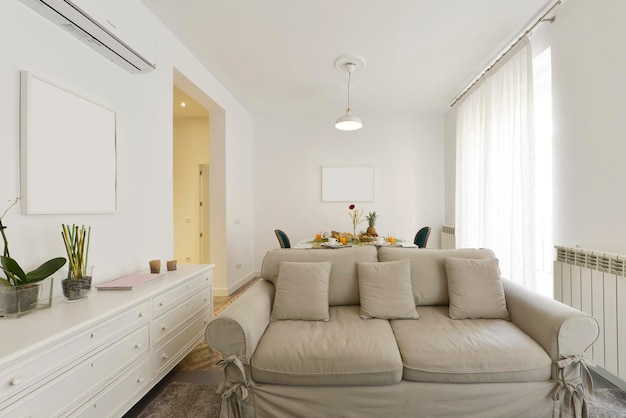 Sala com sofá de dois lugares com janelas de tecido cinza com cortinas brancas e móveis de madeira branca