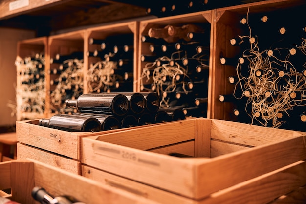 Sala de armazenamento com garrafas de bebida alcoólica em caixas de madeira e prateleiras de vinho com rótulos de ano vintage