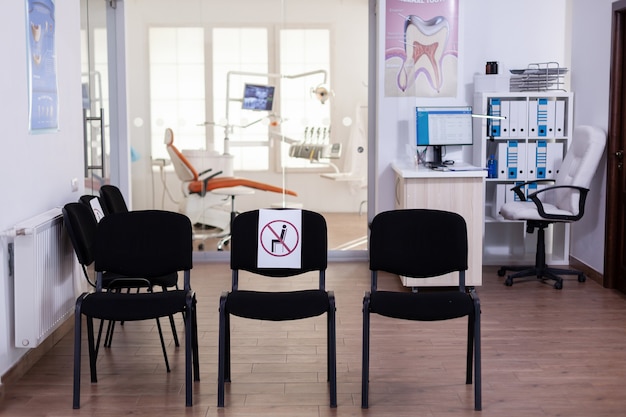 Sala de espera vazia, recepção de estomatologia sem ninguém, com novo sinal na cadeira para distância social durante a epidemia de covid-19