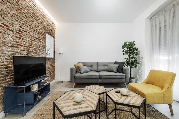 Foto sala de estar com sofá cinza tv mesa de jantar em vidro circular cortinas brancas sofás pessoais amarelos e mesa de tv em metal azul e mesas poliédricas baixas e parede de tijolo aparente