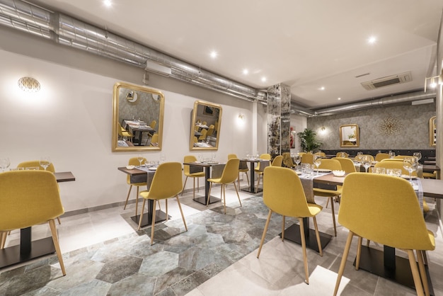 Foto sala de jantar de um restaurante com mesas e cadeiras montadas estofadas em tecido amarelo e tubos de ar condicionado expostos