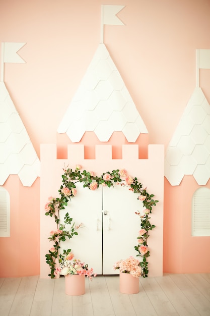 Sala de jogos com um castelo rosa para crianças. Quarto infantil para uma princesinha. Decorações para uma festa infantil. Pequeno apartamento princesa com uma fechadura rosa e porta branca com flores encaracoladas.