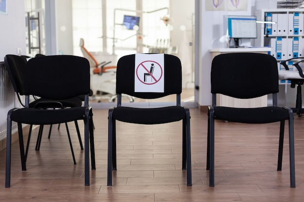 Sala de espera en la clínica sin nadie en ella, oficina principal con nuevo signo normal en la silla para distancia social en la pandemia de coronavirus. Recepción de estomatología vacía durante la epidemia de covid-19.