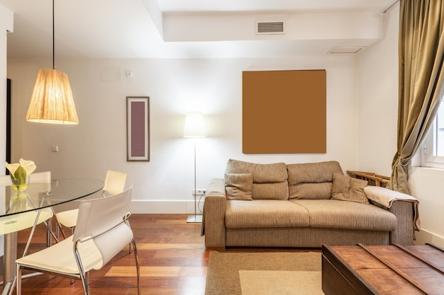 Sala de estar de una casa con muebles de inspiración ecléctica, un sofá de tela gris, un baúl de madera, una mesa de comedor circular de vidrio y un piso de madera rojizo