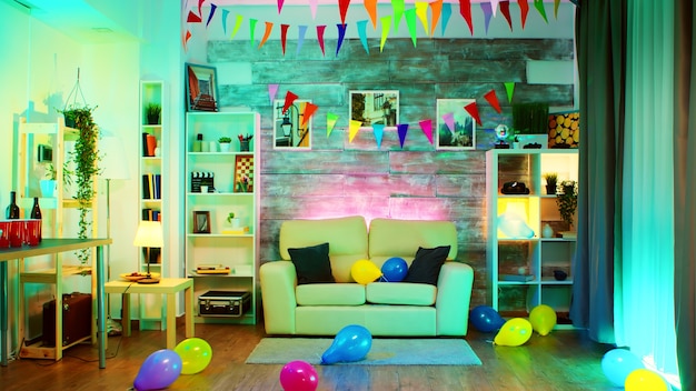 Foto sala de fiesta decorada con luces de neón en la pared y una bola de discoteca, bebidas, globo y papas fritas.