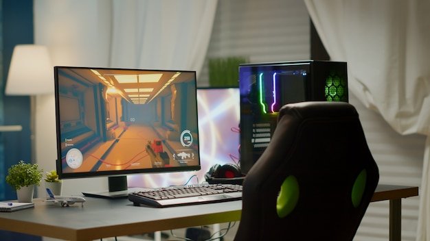 Foto sala vazia com computador pessoal poderoso rgb para videogames online e cadeira de jogos, jogo de tiro em primeira pessoa na tela. este quarto aconchegante com design moderno é iluminado com luz aconchegante e neon.