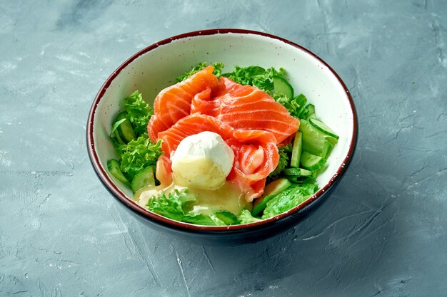 Salada apetitosa com salmão, ovo escalfado, molho holandês e alface em uma tigela branca sobre fundo cinza