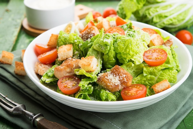 Salada Caesar com filé de frango, tomate, croutons e parmesão em um prato sobre fundo de madeira rústico, close-up