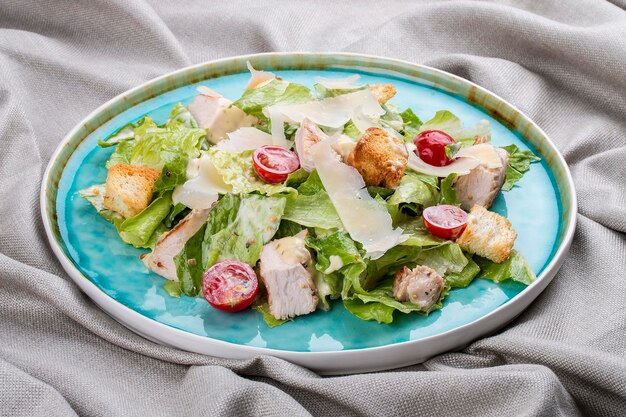 Salada Caesar com frango parmesão e tomate cereja em uma placa azul sobre um fundo têxtil
