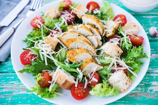 Foto salada caesar com peito de frango em um fundo rústico, tomates, parmesão, salada verde e croutons, foco seletivo, close-up