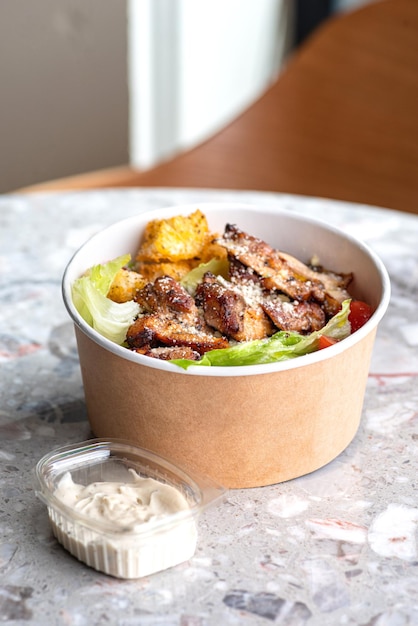 Salada Caesar italiana com parmesão de frango e biscoitos em um recipiente de papelão artesanal para entrega