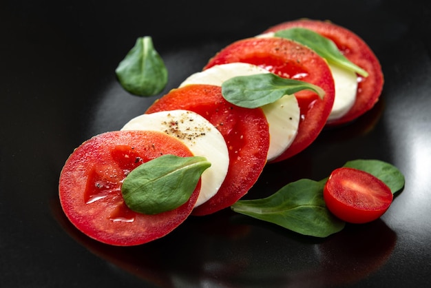 Salada Caprese com azeite de tomate e queijo mussarela e pimenta preta Salada italiana em um prato preto com queijo e tomate Cozinha Europeia