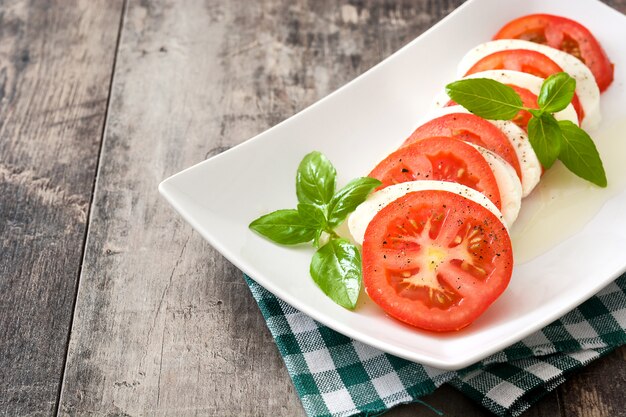 Salada Caprese com tomate mussarela e manjericão em madeira rústica, cópia espaço