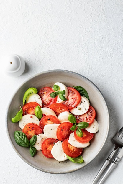 Salada caprese italiana com tomate fatiado mussarela manjericão azeite com talheres e saleiro em fundo branco com espaço de cópia Vista superior