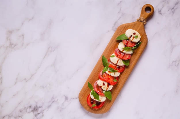 Salada caprese italiana com tomate fatiado, mussarela, manjericão, azeite em uma tábua de madeira.