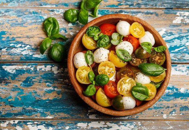 Salada caprese italiana com tomate fatiado, queijo mussarela, manjericão, azeite de oliva em uma tigela de madeira.