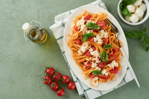 Salada caprese ou macarrão espaguete quebrado com manjericão e mussarela ala caprese na chapa branca sobre fundo verde de madeira rústica Cozinha italiana tradicional Conceito de comida italiana Receita de vista superior