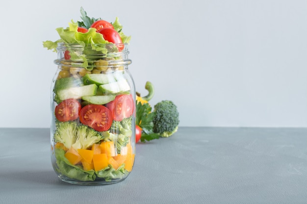 Salada caseira vegetal no frasco de pedreiro com tomate, alface, brócolis no azul. Copie o espaço. Almoço para o trabalho. Comer limpo.