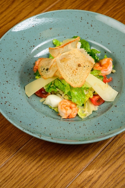 Salada César com camarão na placa azul em fundo de madeira. Salada César com camarões, vista superior