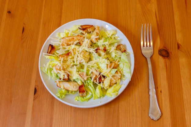 Salada César fresca e saudável com peito de frango, alface, molho de queijo parmesano e croutons em mesa de madeira