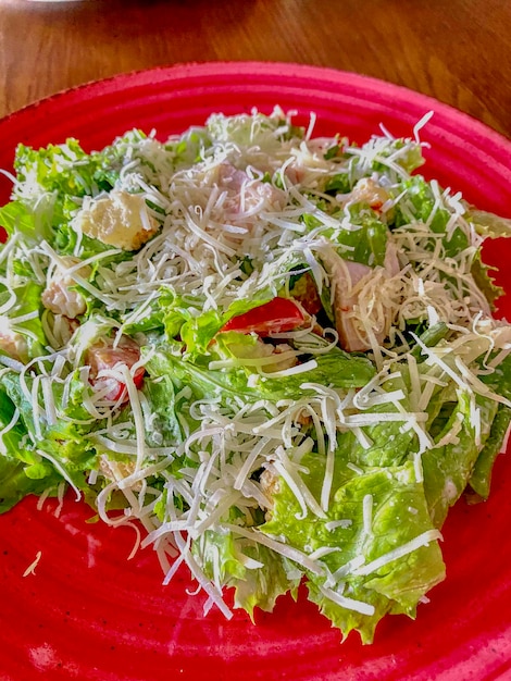 Foto salada césar con jamón y queso en un plato rojo de cerca