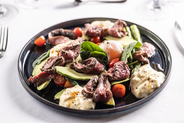 Salada colorida com fraldinha enchendo o prato escuro em uma mesa de restaurante