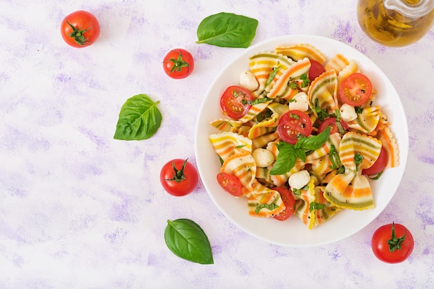 Foto salada colorida do farfalle da massa com tomates, mussarela e manjericão.