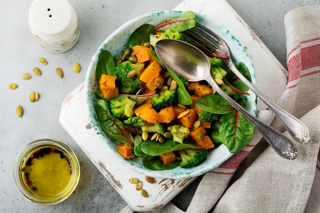 Salada com abóbora assada, acelga, brócolis e sementes de abóbora em placa de cerâmica na pedra ou mesa de concreto. estilo rústico.