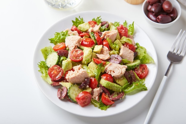 Salada com atum alface pepinos tomates azeitonas e abacates em chapa branca em cima da mesa