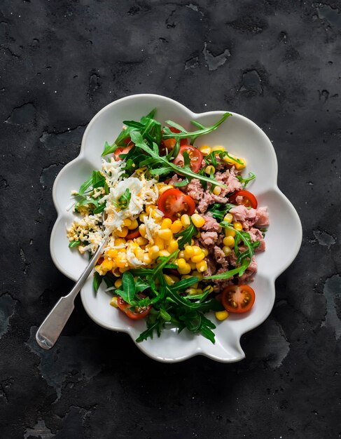 Salada com atum enlatado, ovo cozido, rúcula, tomate cereja e milho em uma vista superior de fundo escuro