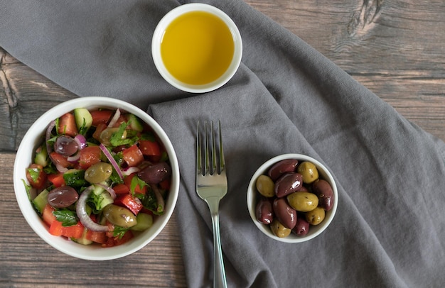 Salada com azeitonas kalamata e azeite em fundo de madeira com têxtil cinza