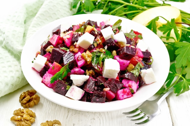 Salada com beterraba, queijo feta salgado, maçãs, nozes, salsa, temperada com vinagre balsâmico e azeite de oliva em um prato, uma toalha e um garfo sobre um fundo de tábua de madeira