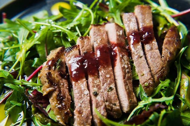 Salada com bife, rúcula e acelga em uma placa preta.