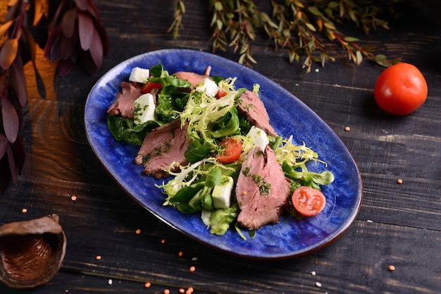 Salada com carne, alface, tomate cereja e queijo. No prato azul