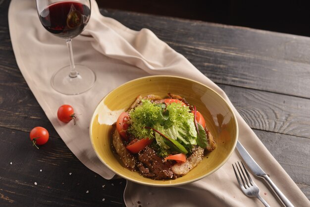 Salada com carne, tomate, sementes de gergelim e alface. Em um prato amarelo em uma mesa de madeira