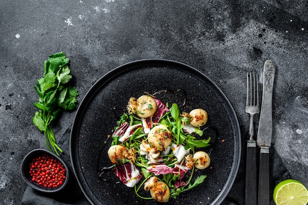 Salada com choco grelhado e rúcula. Superfície preta. Vista do topo. Copie o espaço