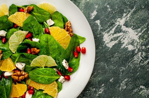 salada com espinafre, laranja, limão, romã, queijo feto, nozes em um prato branco no contexto da ardósia, pedra ou concreto