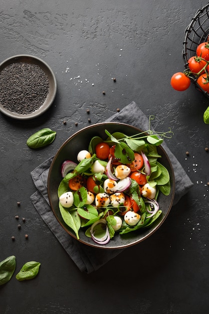 Salada com espinafre, legumes de verão e mussarela em fundo preto. Vista do topo.