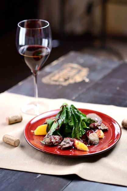 Salada com fígado, espinafre e laranja em um prato vermelho, em uma mesa de madeira