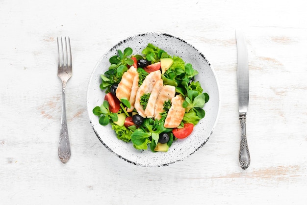 Salada com filé de frango azeitonas tomates e abacates em um prato com fundo de madeira Vista superior Espaço livre para o seu texto Postura plana