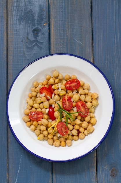 Salada com grão de bico e tomate na chapa branca na superfície azul