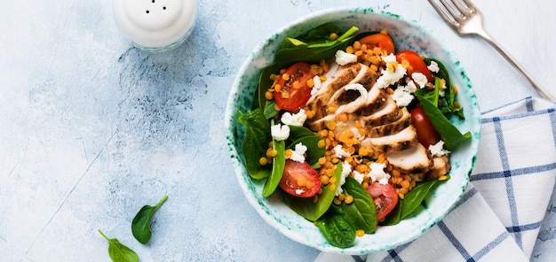 Salada com lentilhas vermelhas, folhas de espinafre, tomate cereja, carne de frango e queijo mussarela com azeite em placa de cerâmica no antigo fundo cinza de concreto.