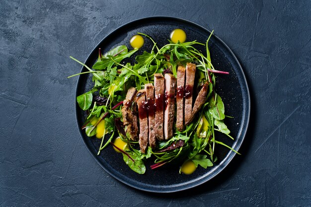 Salada com lombinho de carne, rúcula e acelga em uma placa preta.