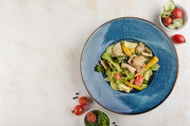 Salada com Lula. Alface, abobrinha, mini milho, tomate, lula e molho em uma placa azul sobre um fundo claro. Vista superior com um espaço de cópia para o texto. Orientação horizontal.