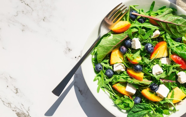 Salada com nectarinas, mirtilos, rúcula, espinafre e queijo feta em fundo de mármore branco