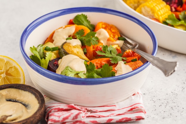 Salada com os vegetais cozidos com o tahini na placa branca, fundo branco. Conceito de comer limpo.