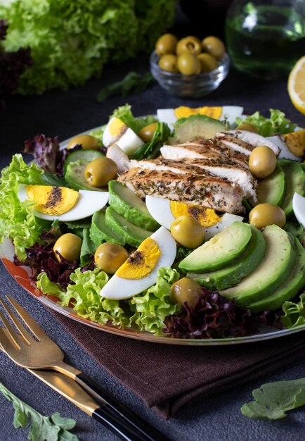 Salada com ovos de frango abacate e azeitonas temperadas com limão e azeite servido em folhas de alface em fundo cinza