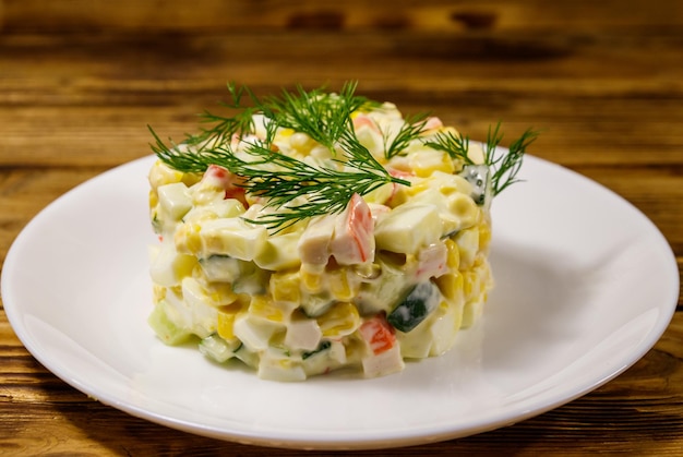 Salada com palitos de caranguejo, ovos de pepino de milho doce e maionese na mesa de madeira