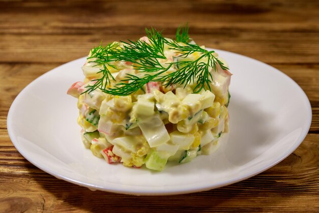 Salada com palitos de caranguejo, ovos de pepino de milho doce e maionese na mesa de madeira