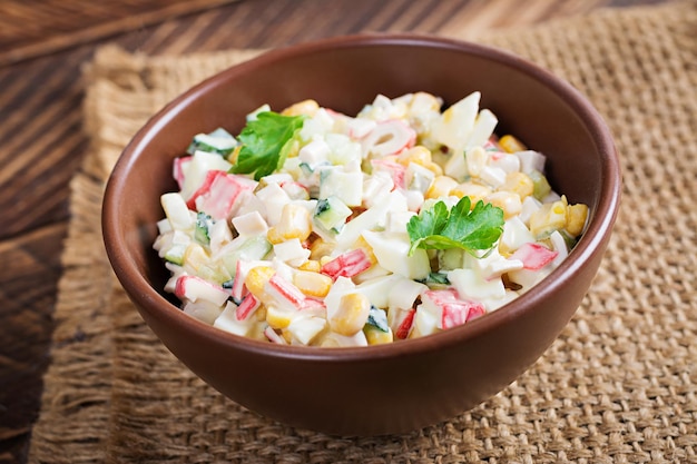 Salada com palitos de milho e caranguejo na tigela na mesa de madeira. cozinha tradicional russa.